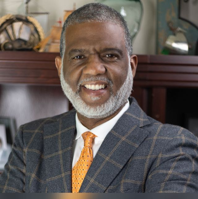 Joe Follette smiling, wearing a navy jacket and orange tie